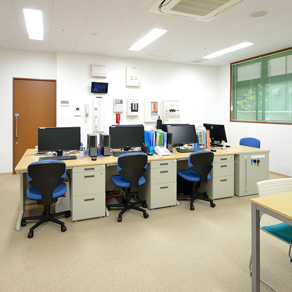 介護施設のスタッフ室。複数のデスク、パソコン、事務機器が配置された明るい作業空間